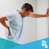 Young man with lower back pain leaning against a wall