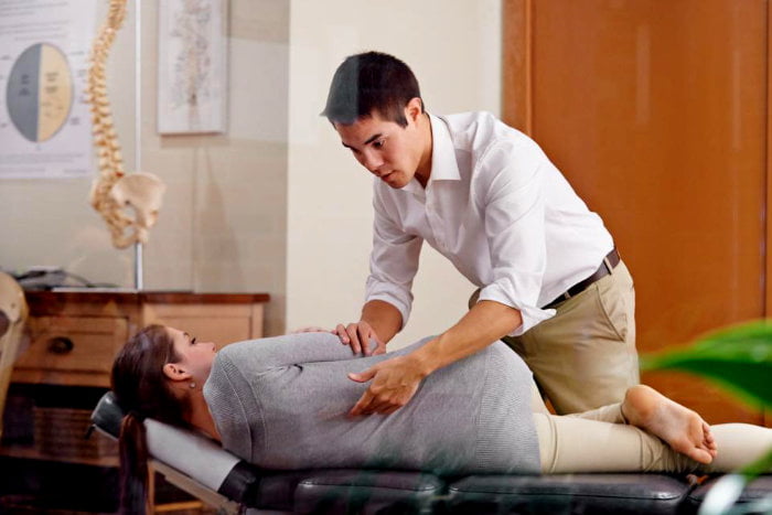 Male chiropractor adjusting a female patient's sore low back