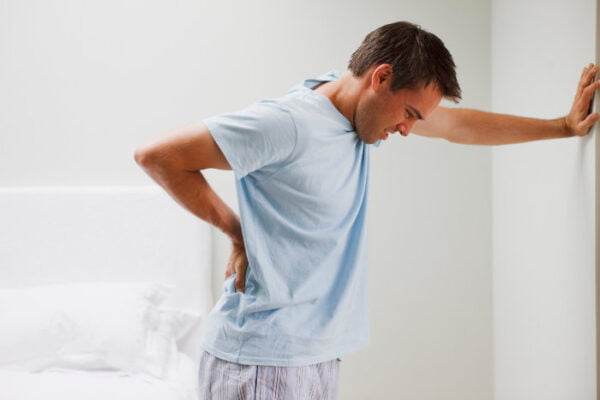 Man with low back pain standing and bracing himself on a wall