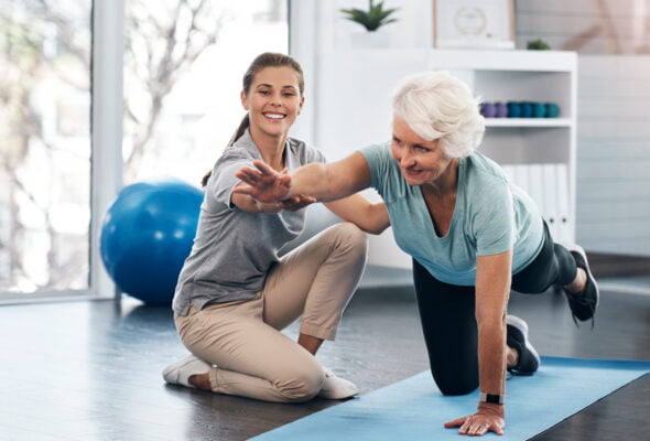 Clinician assisting an elderly female patient with a quadruped exercise on the floor