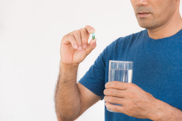 Close up of man taking in pill and another hand holding a glass of clean water