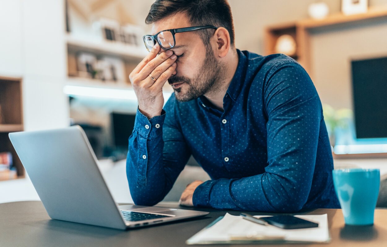 Young male with headache working on a laptop computer