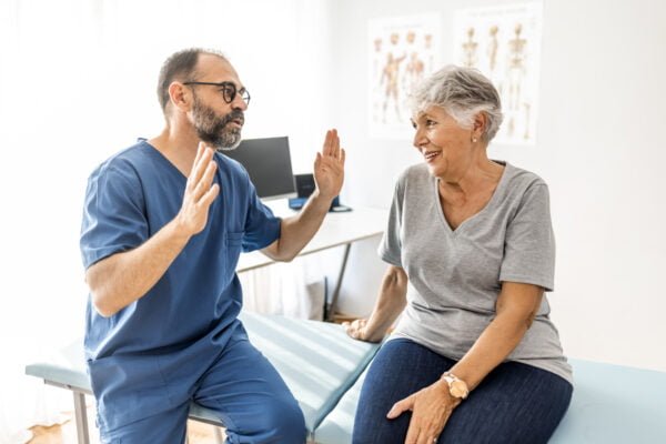 Confident mature male chiropractor talks with elderly female patient