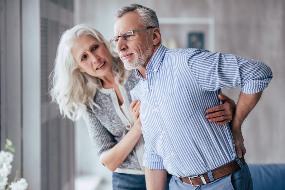 Senior woman helping her husband who is experiencing back pain