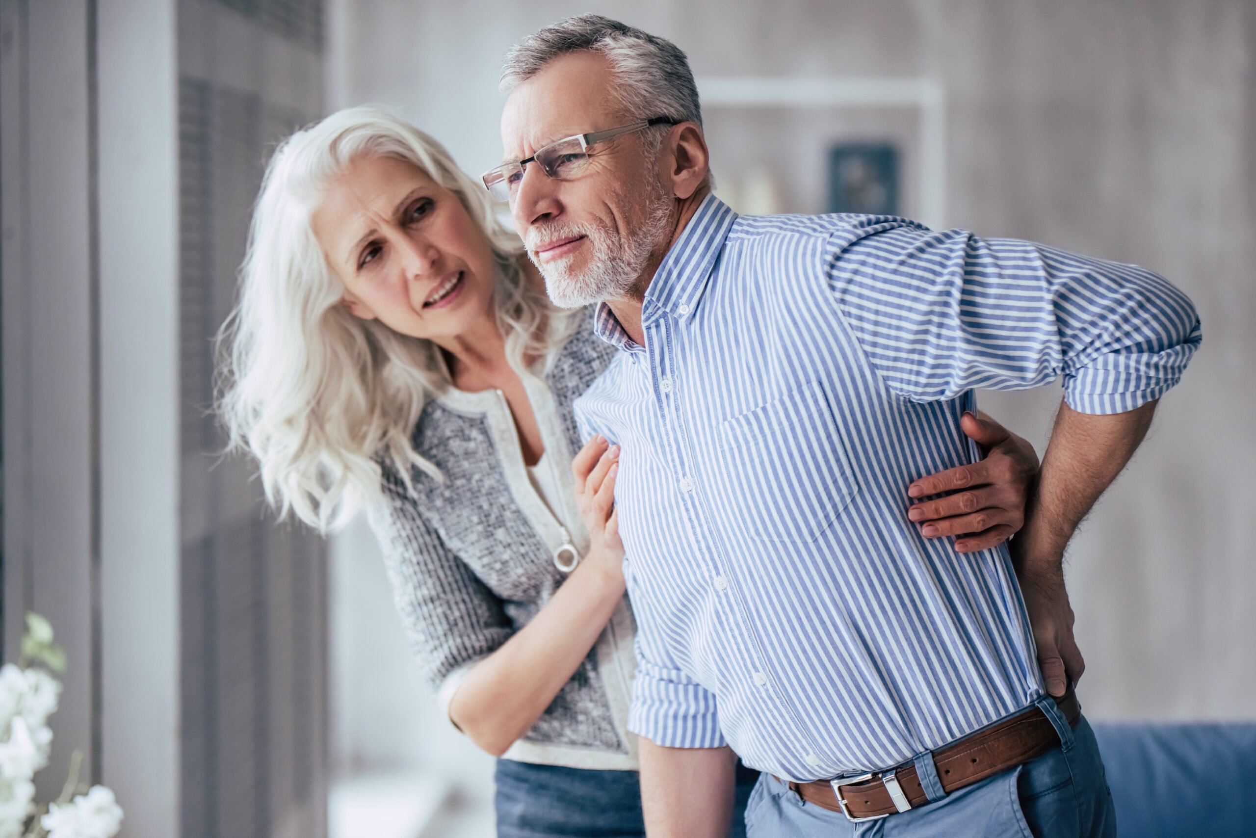 Senior woman helping her husband who is experiencing back pain