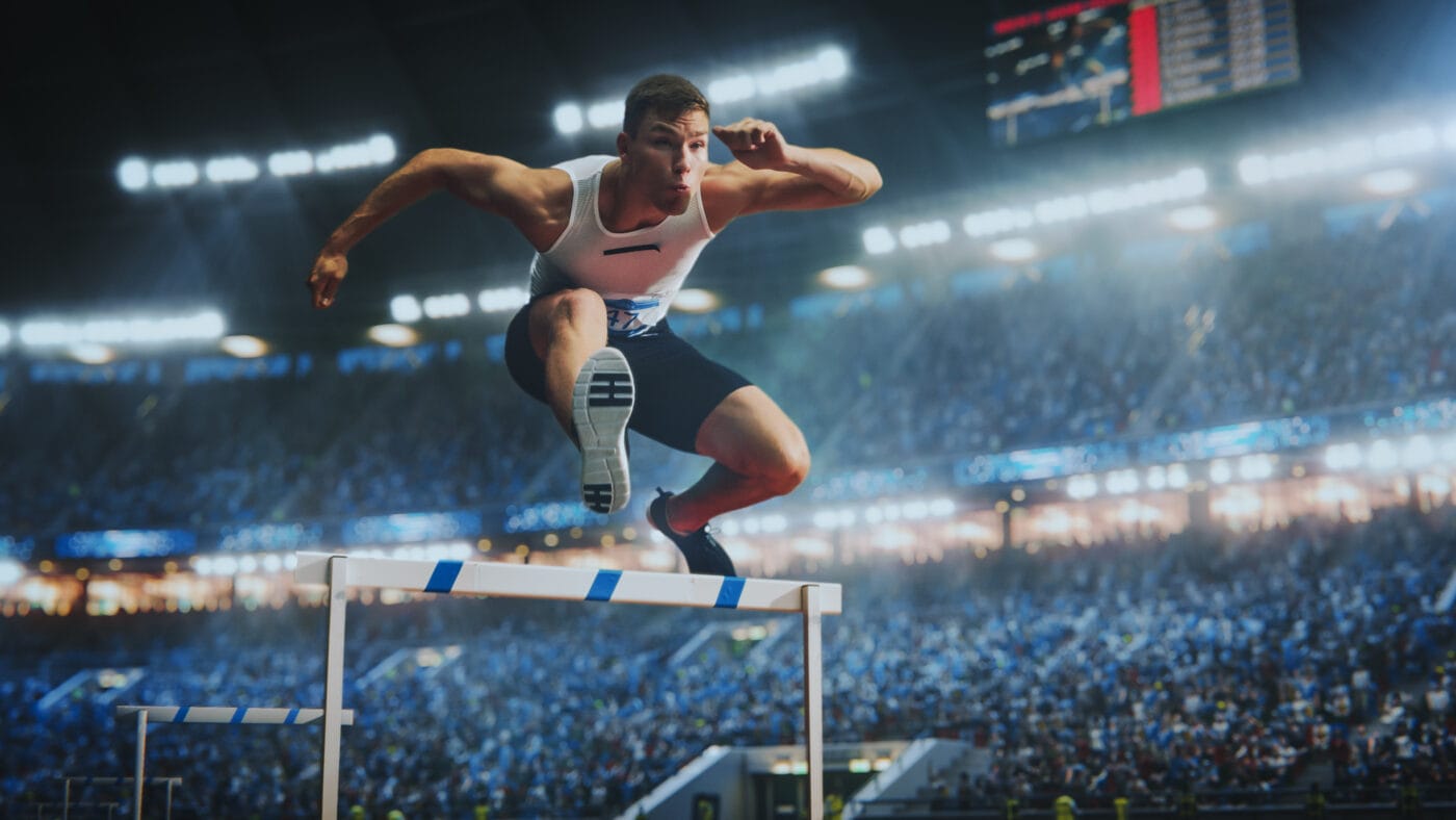 Male hurdler jumping during a race in a big stadium