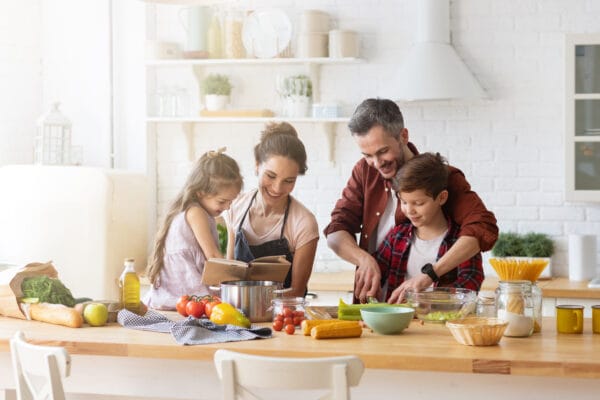 Happy family cooking together in a kitchen. Mother and daughter reading recipe to father and son.