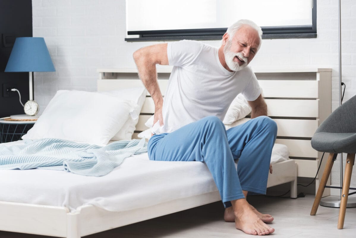 Senior man sitting on his bed suffering from low back pain