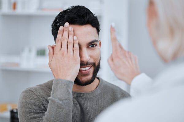 Male patient covering one eye with his hand while following the finger of a female clinician during clinical testing