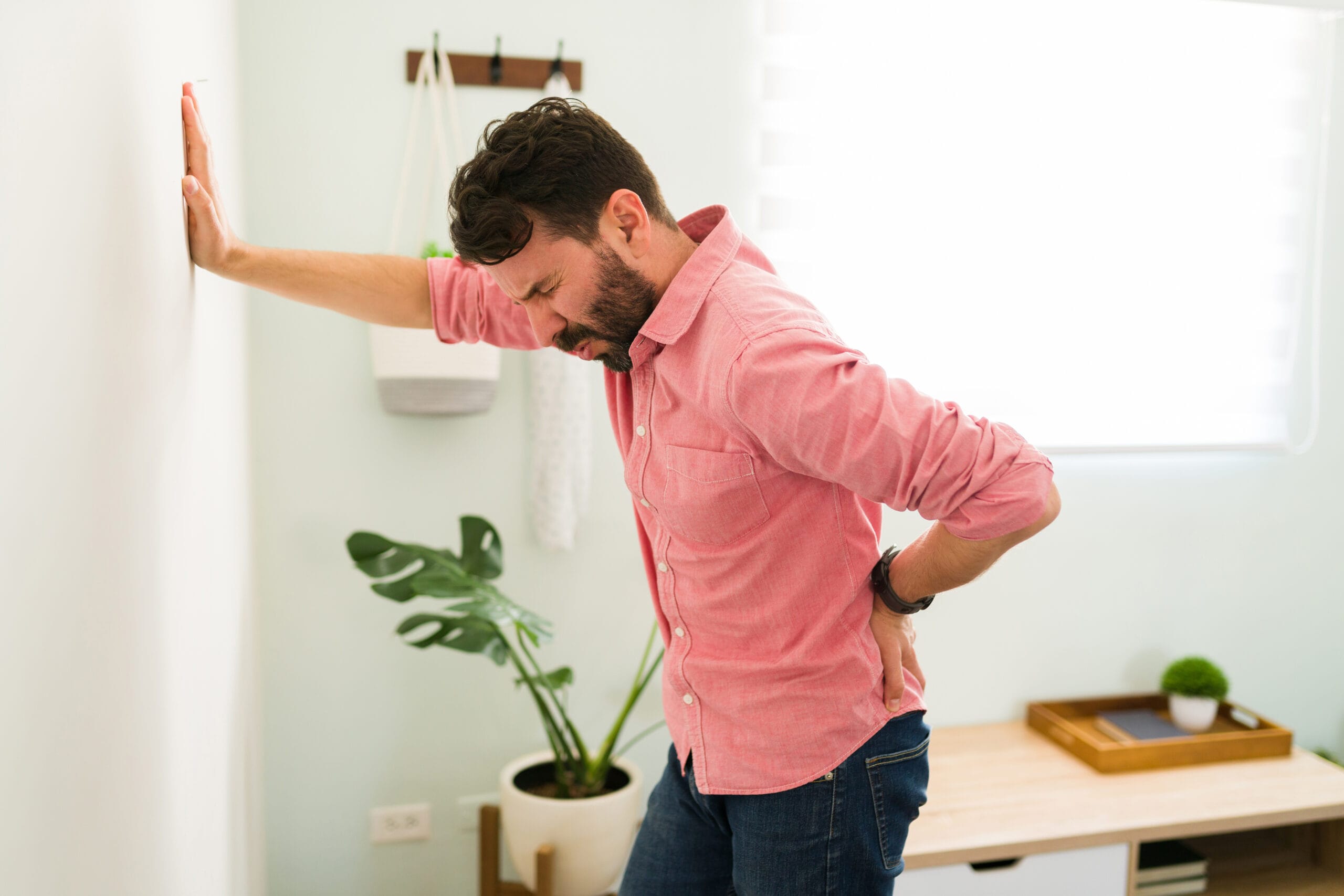 Young man leaning against a wall and wincing due to low back pain