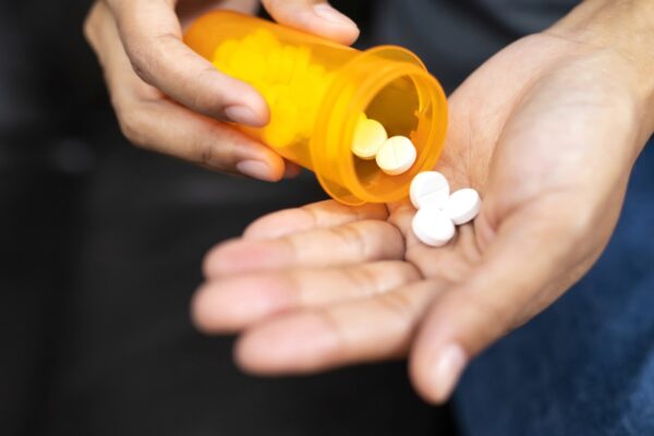 A person putting medication pills in their hand from a small pharmacy bottle