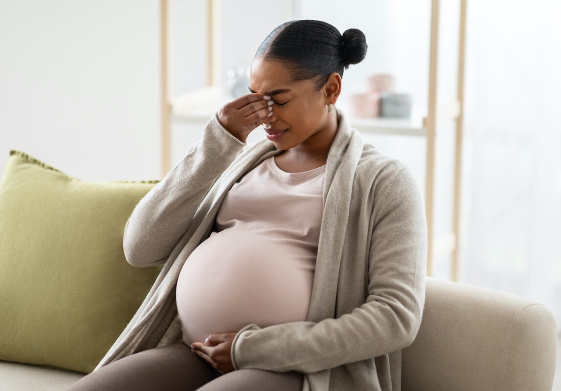 A young black pregnant woman in pain from a migraine headache
